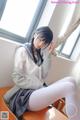 A woman in a school uniform sitting on a desk.