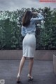 A woman in a white skirt and a blue shirt is standing in the rain.