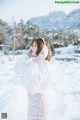 A woman in a white sweater and skirt standing in the snow.