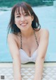 A woman in a white bikini sitting by a swimming pool.