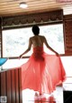 A woman in a long red dress standing in front of a window.