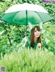 A woman in a green shirt holding an umbrella in the grass.