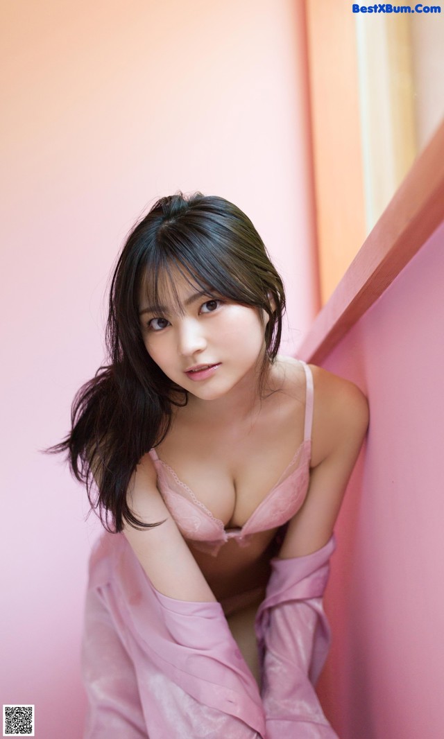 A woman in a pink lingerie leaning against a pink wall.