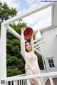 A woman in a white dress and red hat standing on a porch.