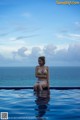 A woman in a bikini sitting on the edge of a swimming pool.