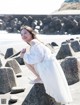 A woman in a white dress sitting on a rock on the beach.